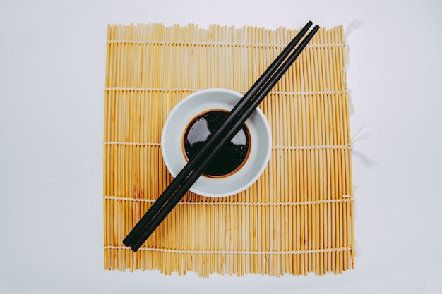 Sauce soja japonaise avec baguettes traditionnelles et tapis de sushi fond blanc isolé