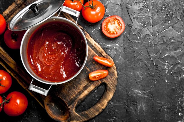 Photo sauce tomate dans une casserole sur une planche à découper et des tranches de tomate