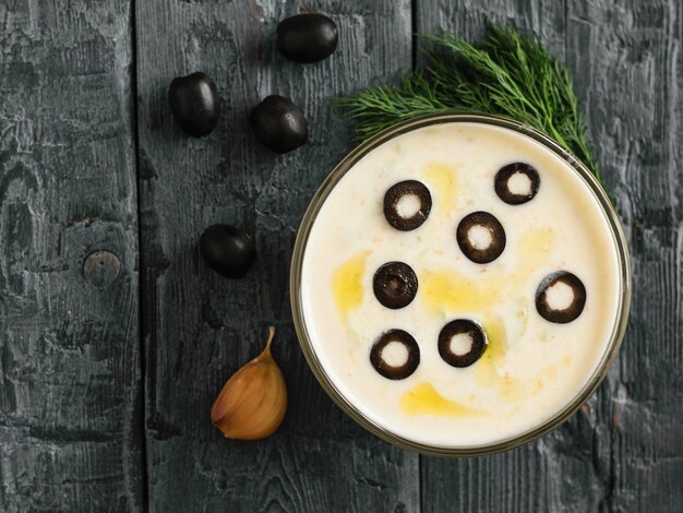 Sauce tzatziki dans un bol en verre sur une table en bois foncé avec une branche d'aneth et d'olives