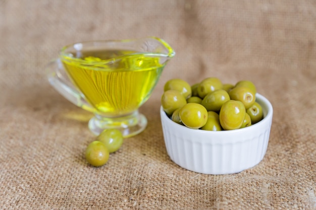 saucière en verre avec de l'huile d'olive extra vierge et des olives vertes fraîches dans un bol en céramique blanche