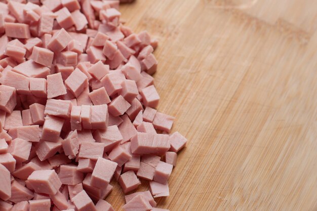 Saucisse bouillie finement coupée en dés de couleur rose sur une planche à découper en bois avec des bords flous