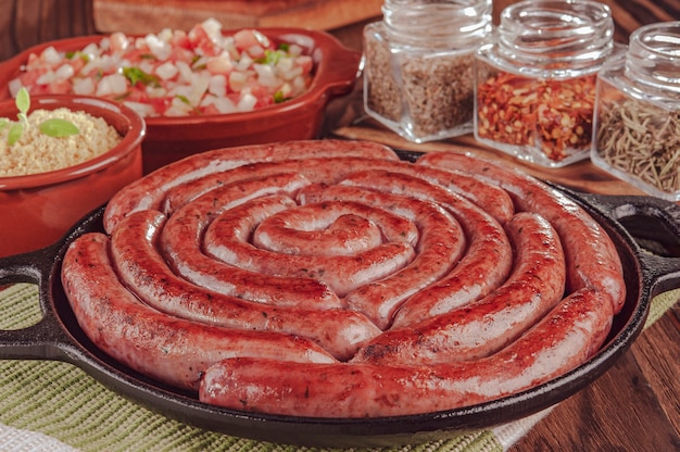 Saucisse brésilienne grillée sur plaque de fer avec salade, farofa et épices