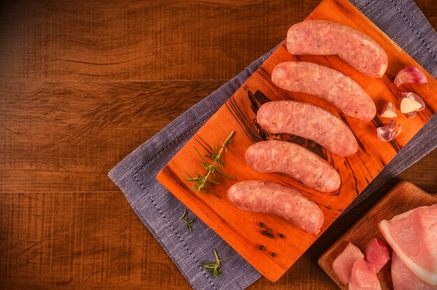 Saucisse de cuisse de porc brésilien à l'ail sur une planche à découper en bois et cuisse de porc isolée sur bois