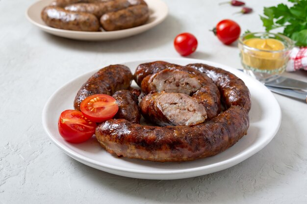 Saucisse cuite maison juteuse sur une assiette avec de la moutarde et des tomates fraîches.