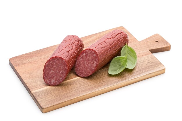 Saucisse fumée au salami, feuilles de basilic sur la découpe de surface blanche.