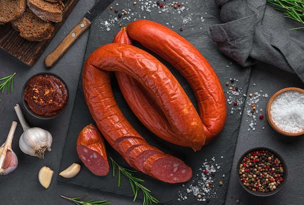 Saucisse fumée de Cracovie aux épices, ail et romarin sur fond noir. Vue de dessus, horizontale.