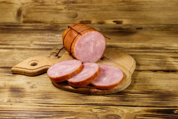 Saucisse fumée tranchée sur une planche à découper sur une table en bois