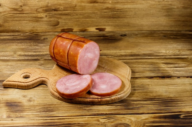 Saucisse fumée tranchée sur une planche à découper sur une table en bois