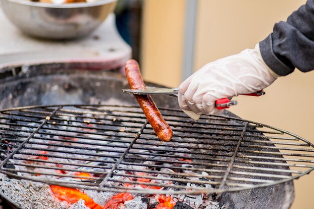 Saucisse grillée sur un feu ouvert La main tourne la saucisse avec des pinces