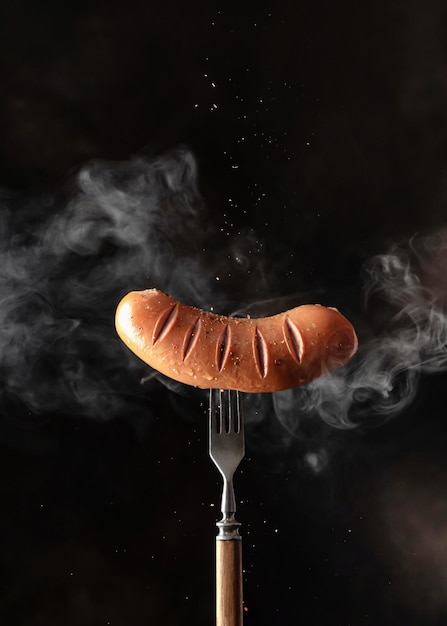 Photo saucisse grillée rôtie savoureuse unique avec des épices saupoudrées sur une fourchette rustique sur fond noir foncé avec espace de copie de vapeur