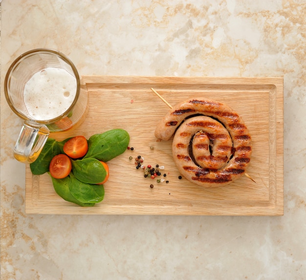 Saucisse grillée en spirale avec chope de bière, épinards et tomates