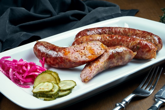 Saucisse hachée juteuse de porc juteux cuit dans un fumoir avec du cheddar dans une assiette blanche avec des légumes en conserve. Collation de bière allemande