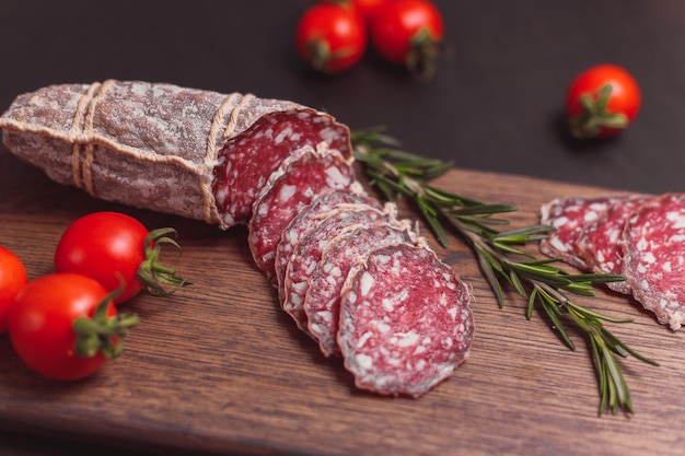 Saucisse de jambon fumé et tranches coupées avec romarin et tomates cerises sur planche de bois foncé