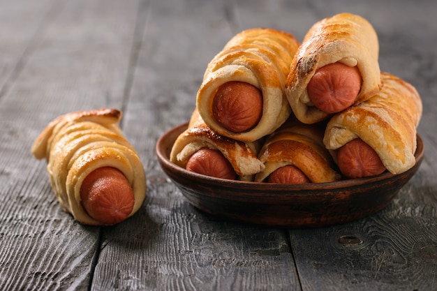 Saucisse maison fraîchement cuite roule dans un bol en argile sur une table en bois rustique.