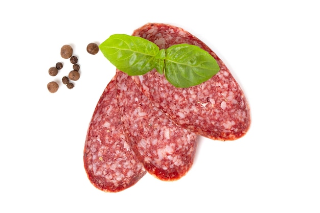 Saucisse de salami fumé séché au boeuf tranché avec des feuilles de basilic et des pois poivrons isolés sur fond blanc