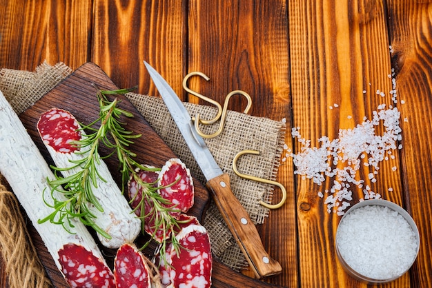 Saucisse séchée en tranches avec des épices et un brin de romarin sur fond rustique en bois.