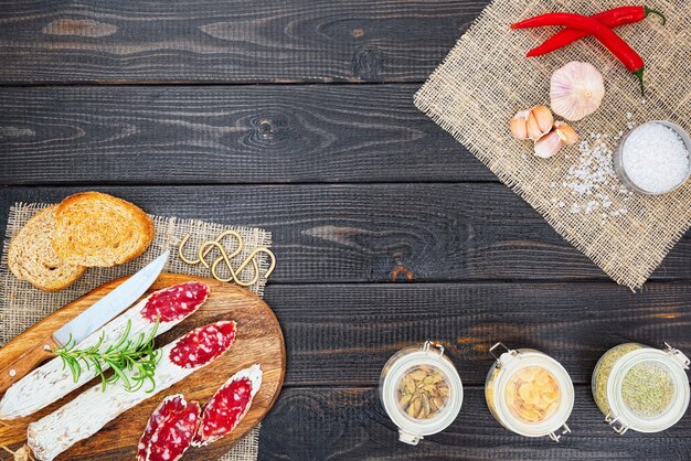 Saucisse séchée en tranches avec des épices un brin de romarin et de pain italien sur fond rustique en bois foncé.