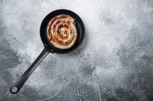 Saucisse en spirale grillée dans une poêle en fonte, sur fond gris, vue de dessus à plat, avec un espace pour le texte copyspace