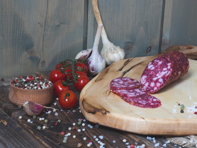 Saucisse tranchée sur une planche de bois avec tomates à l'ail et poivre Saucisse et épices sur une vieille table en bois