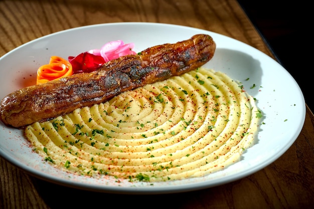 Saucisse de viande bavaroise avec une garniture d'oignons de purée de pommes de terre dans une assiette sur un fond de bois bratwurst