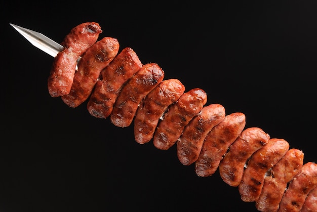 Saucisses barbecue sur des brochettes sur fond noir.