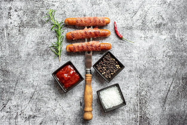 Saucisses sur un bâton avec un bol de poivron rouge et de sel sur fond gris.