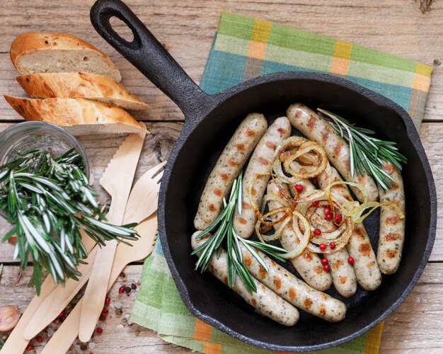 Saucisses blanches frites au romarin, à l'ail et à l'oignon dans une poêle en fonte