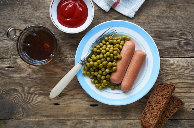 Saucisses bouillies avec des pois verts en conserve sur une plaque