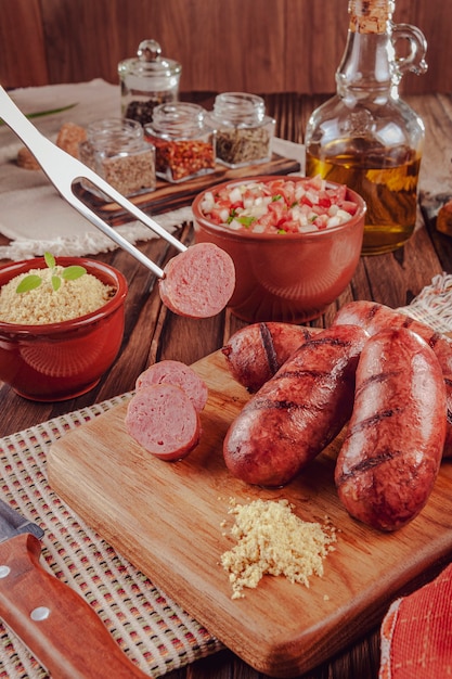 Saucisses brésiliennes grillées sur la planche de bois avec salade, farofa et ingrédients