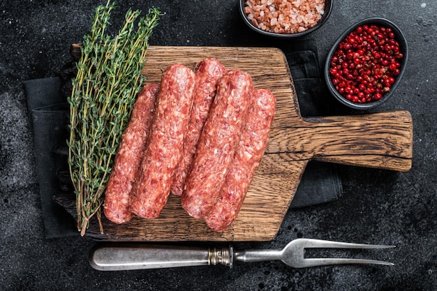 Saucisses de brochettes de viande de boeuf et d'agneau crues non cuites sur une planche de bois. Fond noir. Vue de dessus.