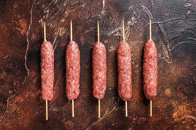 Saucisses de brochettes de viande kofta crues sur des brochettes. Fond sombre. Vue de dessus.