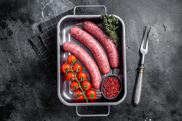 Saucisses crues d'agneau et de viande de bœuf non cuites dans un plateau de cuisine avec des herbes Fond noir Vue de dessus