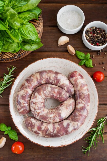 Saucisses crues sur une assiette avec des épices et des herbes fraîches sur un fond en bois foncé Vue de dessus copie espace