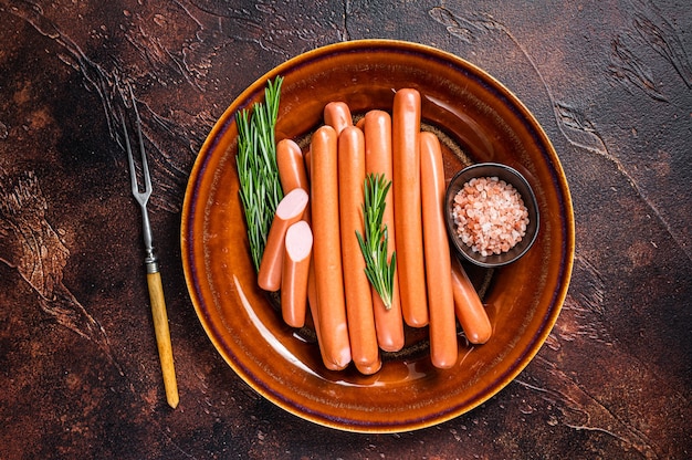 Saucisses crues Frankfurter dans une assiette rustique avec des herbes