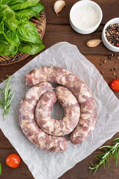 Saucisses crues sur papier avec épices et herbes fraîches sur fond de bois foncé. Vue de dessus, copiez l'espace.