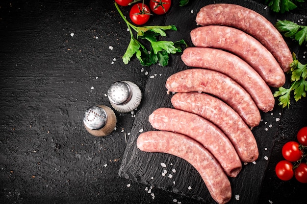 Saucisses crues sur une planche en pierre avec des épices, des tomates et des herbes