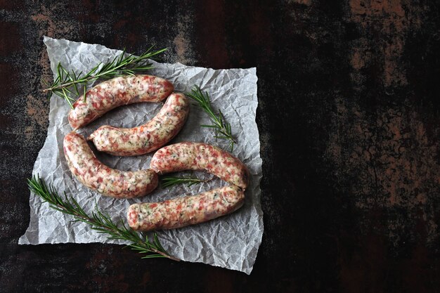 Saucisses crues pour griller au romarin sur papier. Vue de dessus.