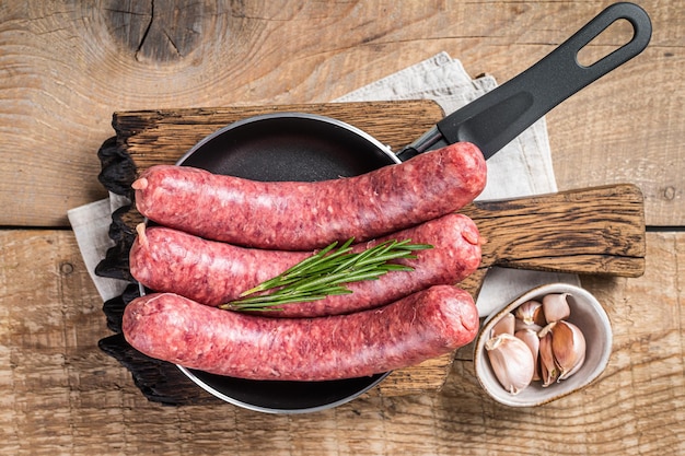 Saucisses crues prêtes à cuire dans une poêle Viande non cuite Fond en bois Vue de dessus