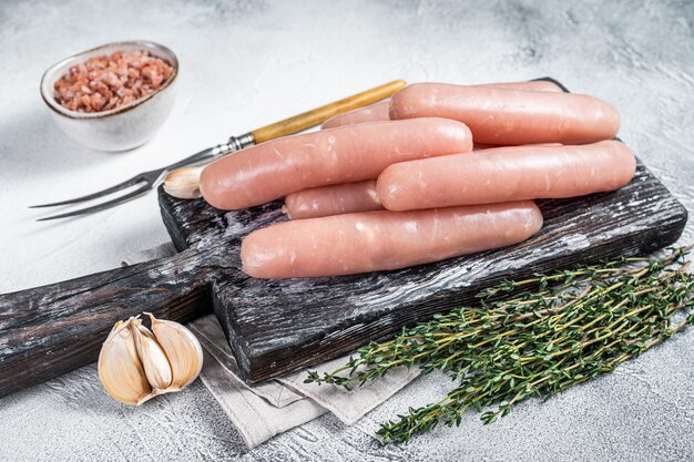 Saucisses crues de viande de poulet et de dinde sur une planche en bois avec du thym. Fond blanc. Vue de dessus.