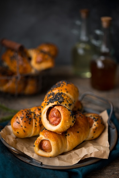 Saucisses cuites dans la pâte et saupoudrées de sésame noir sur fond gris.