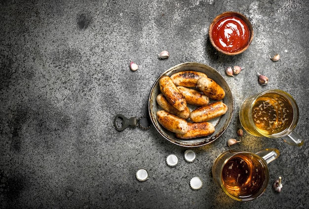 Saucisses dans une poêle avec une bière froide sur table rustique.