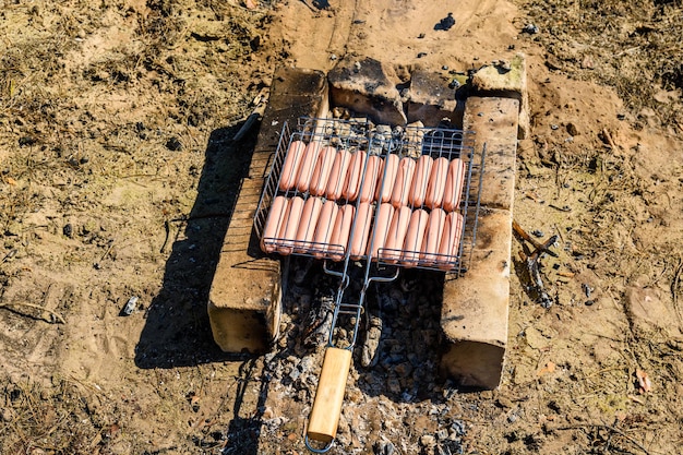 Saucisses faisant cuire dans un gril de barbecue sur le feu de camp