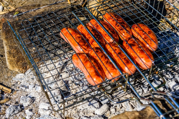 Saucisses faisant cuire dans un gril de barbecue sur le feu de camp