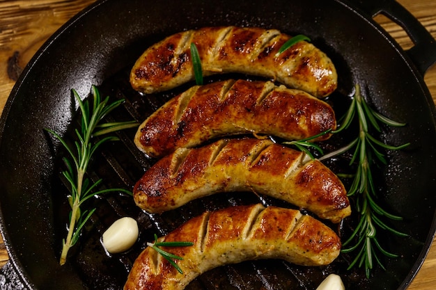 Saucisses frites à l'ail et au romarin dans une poêle à frire en fonte