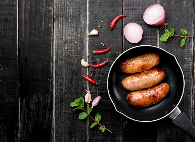 Photo saucisses frites aux herbes dans une poêle à frire sur bois noir, vue de dessus