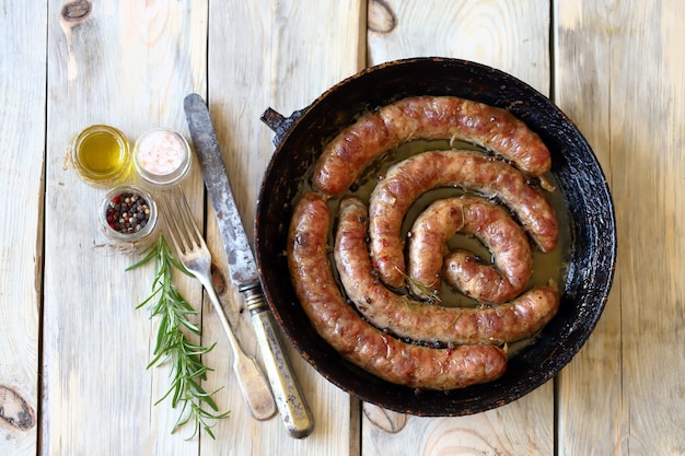 Saucisses frites maison dans une poêle sur une surface en bois.