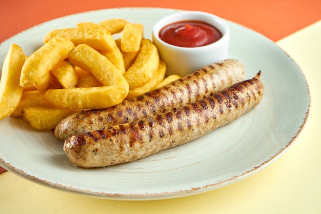 Saucisses grillées allemandes classiques avec frites et sauce rouge dans une assiette blanche sur une surface colorée.