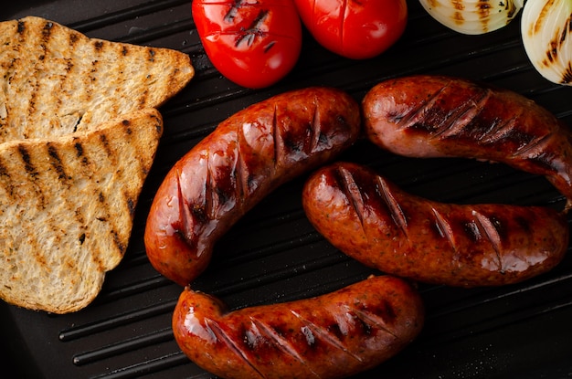 Saucisses grillées au barbecue avec tomates, oignons et toasts dans une poêle à griller. Tir aérien.