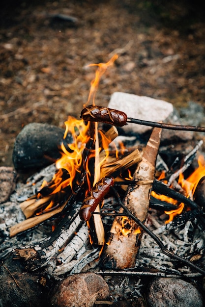 Saucisses grillées au-dessus du feu de camp dans la forêt d'été