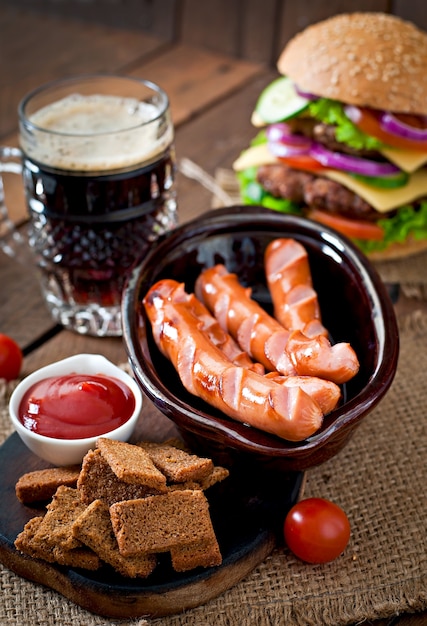 Saucisses grillées, craquelins et bière sur une table en bois de style rustique.